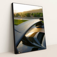 This photo shows a Porsche GT wing and rear vents at sunset with greenery and hills in the background, in a black frame.