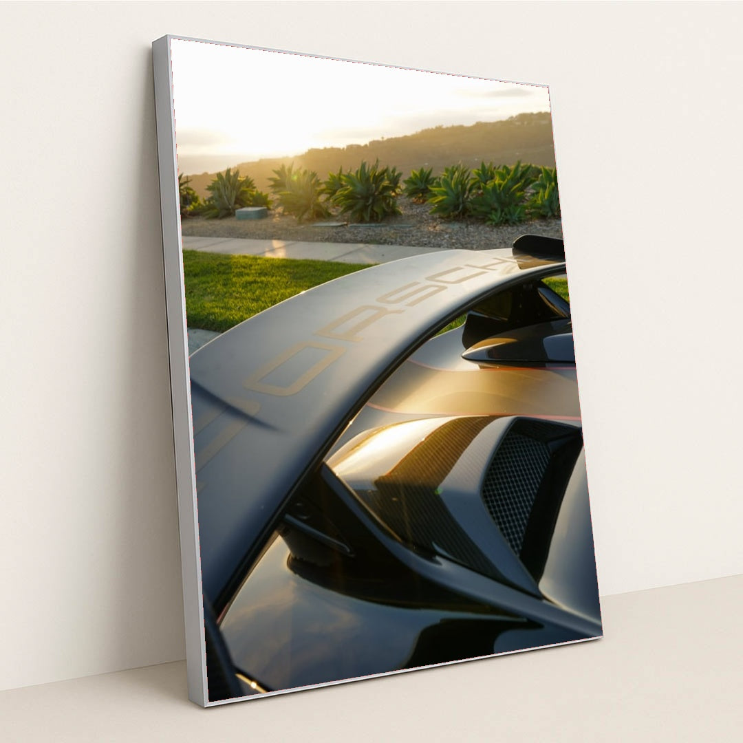 This photo shows a Porsche GT wing and rear vents at sunset with greenery and hills in the background, in a silver frame.