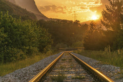 Krivec Ales - Golden sunset over railway tracks surrounded by lush greenery and mountains.