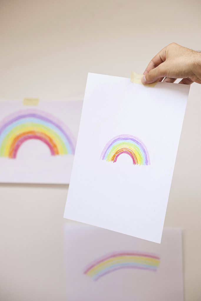 Cup of  Couple - A hand holding a sheet of paper with a colorful rainbow drawing, showcasing creative artwork.