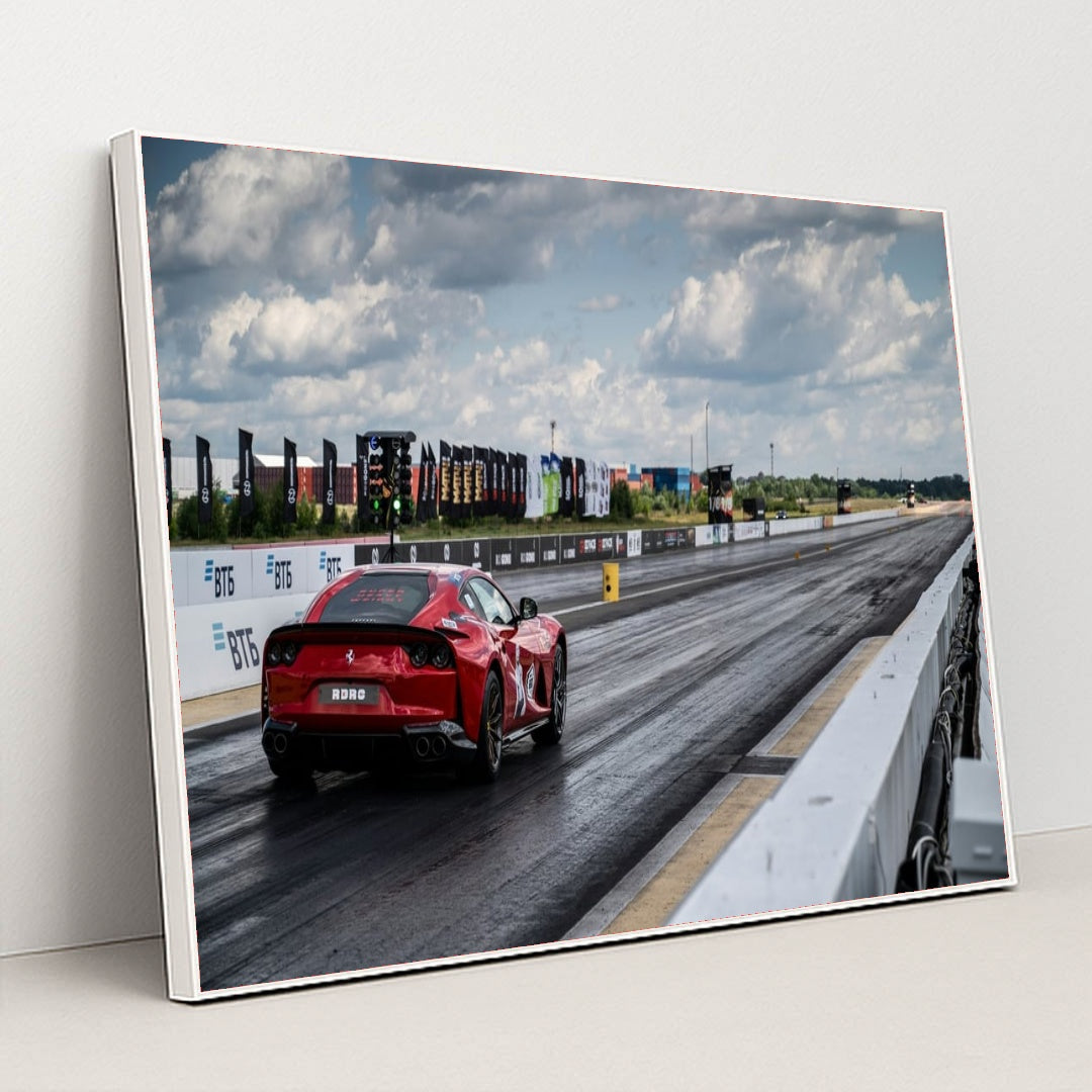 This photo shows a red Ferrari sports car on a dragstrip under a cloudy sky, ready to accelerate, in a white frame.