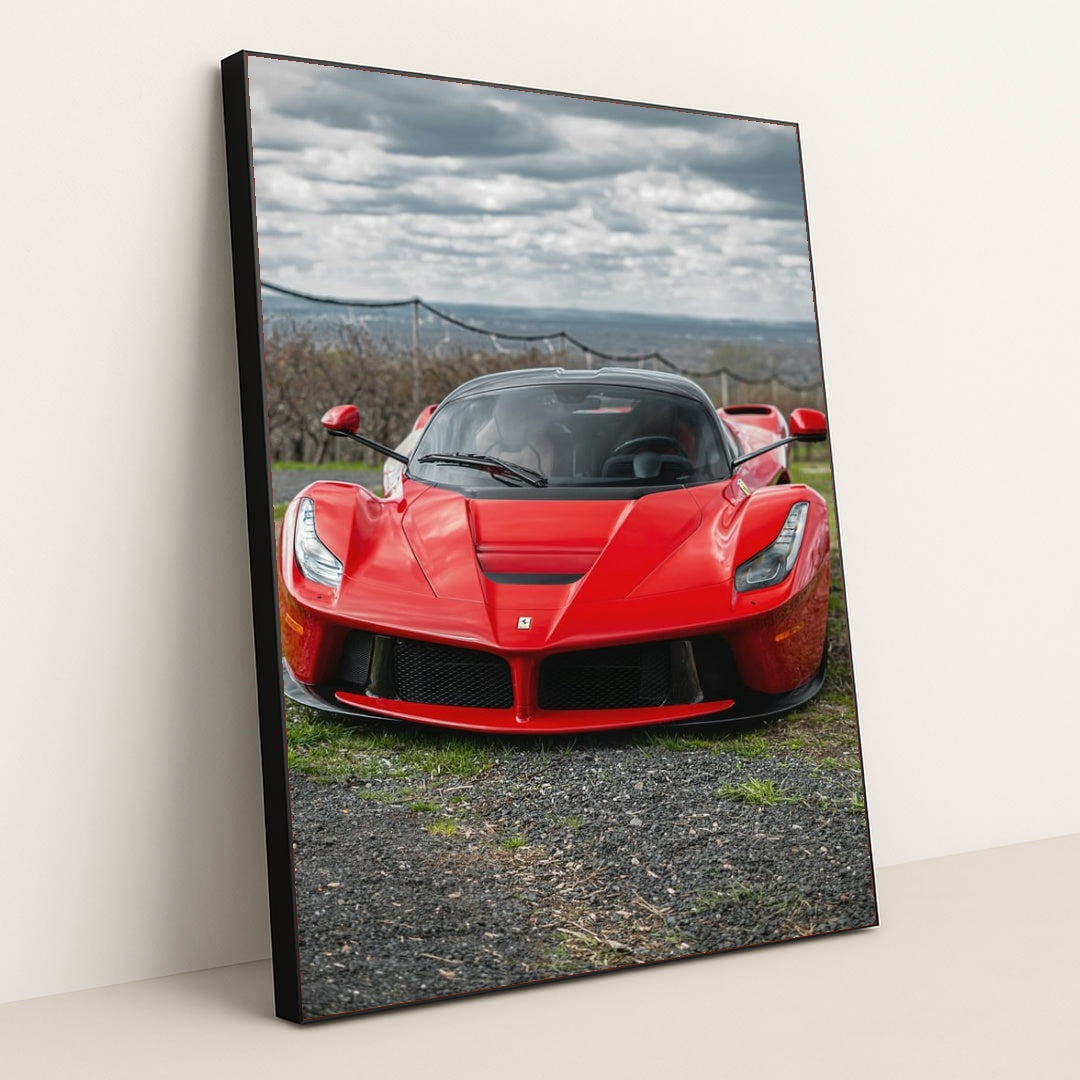 This photo shows a red Ferrari LaFerrari viewed from the front, parked outdoors under a cloudy sky, in a black frame.