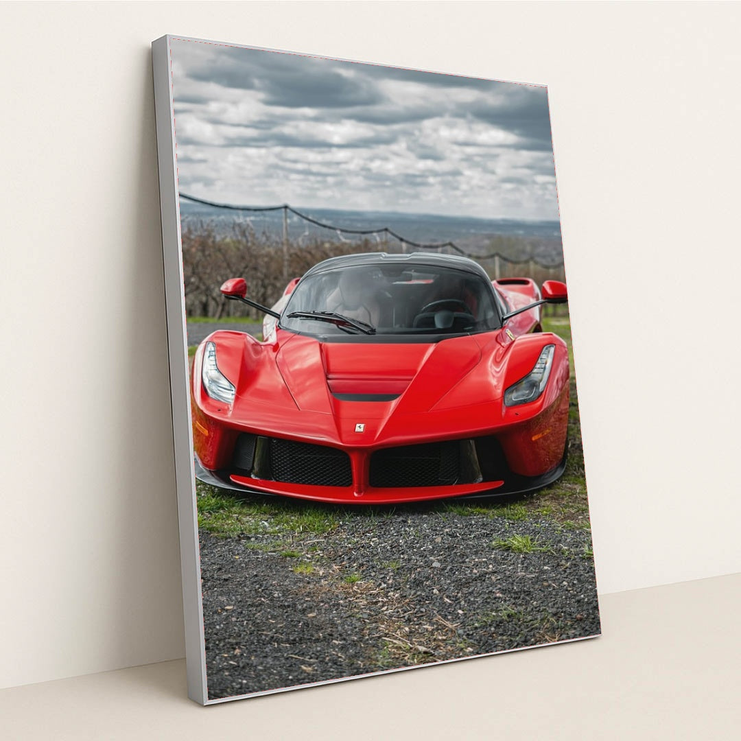 This photo shows a red Ferrari LaFerrari viewed from the front, parked outdoors under a cloudy sky, in a silver frame.