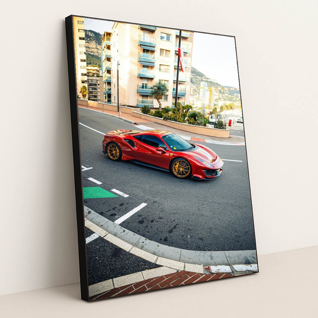 This photo shows a red Ferrari 488 Pista with gold wheels driving through a city street with Mediterranean buildings, in a black frame.