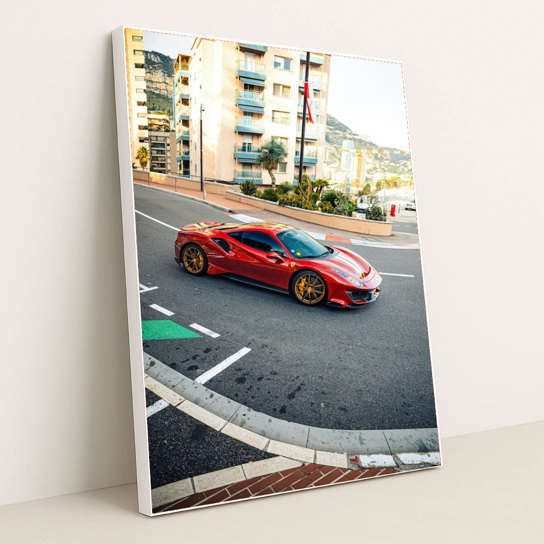 This photo shows a red Ferrari 488 Pista with gold wheels driving through a city street with Mediterranean buildings, in a white frame.