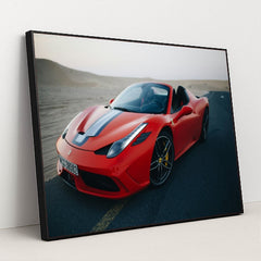 This photo shows a red Ferrari convertible with a blue-and-white racing stripe parked on an empty desert road at dusk, in a black frame.