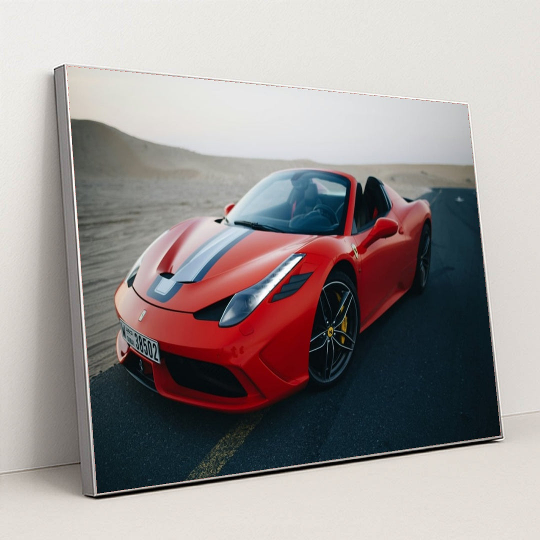 This photo shows a red Ferrari convertible with a blue-and-white racing stripe parked on an empty desert road at dusk, in a silver frame.