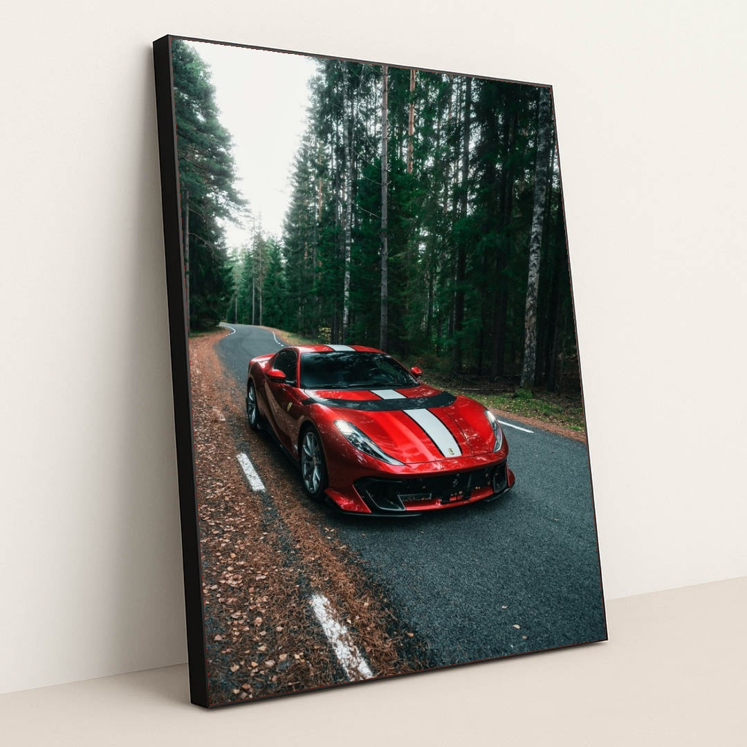 This photo shows a red Ferrari 812 Competizione with a white racing stripe parked on a winding forest road, in a black frame.