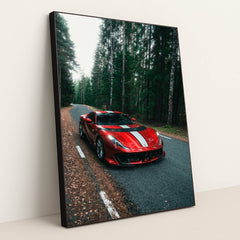This photo shows a red Ferrari 812 Competizione with a white racing stripe parked on a winding forest road, in a black frame.