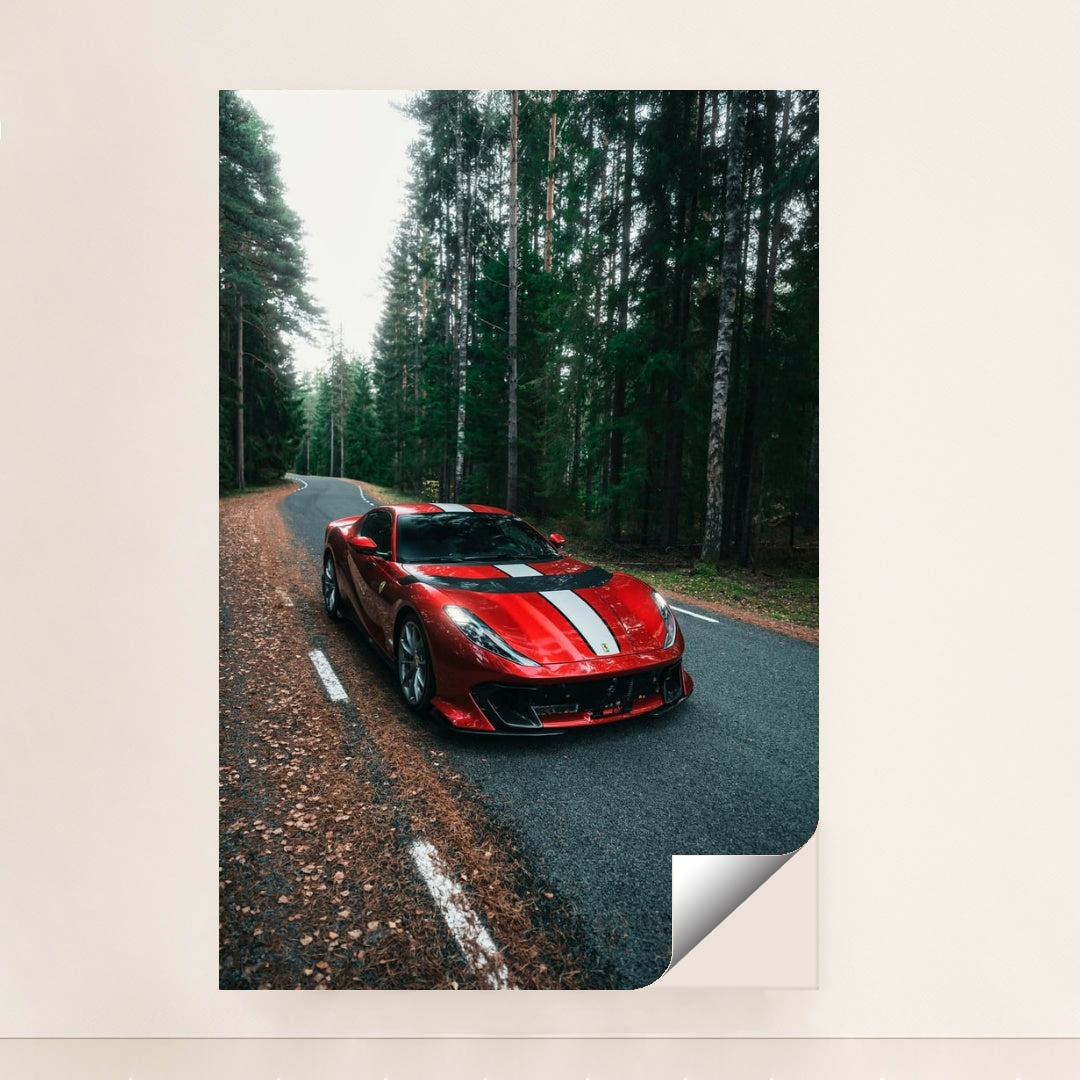 This photo shows a red Ferrari 812 Competizione with a white racing stripe parked on a winding forest road, unframed style.