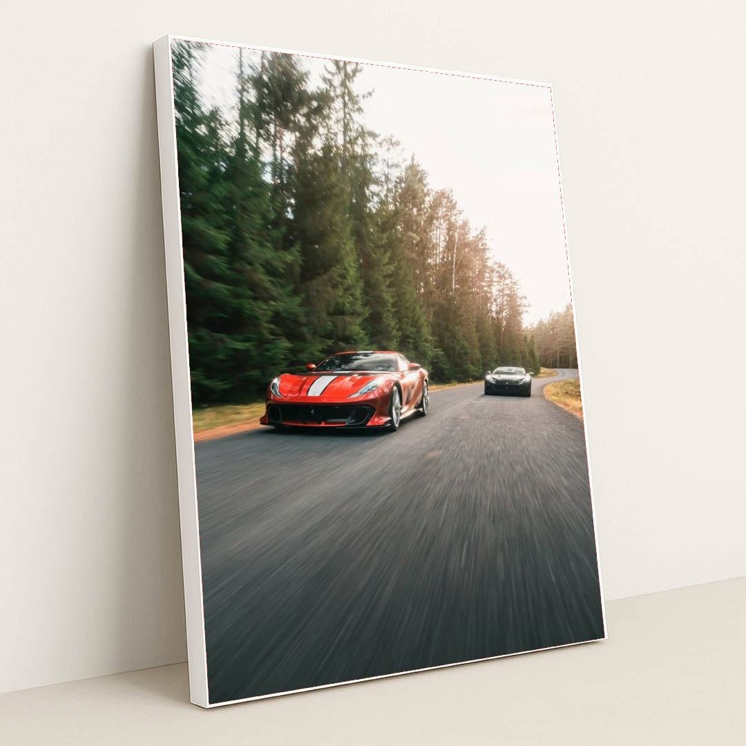 This photo shows a red Ferrari sports car with white stripes leading another car on a winding forest road, in a white frame.