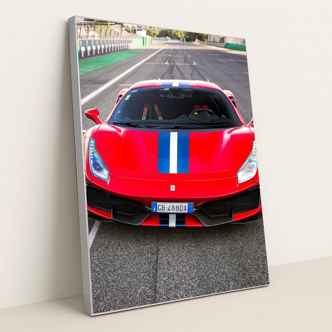 This photo shows the front view of a red Ferrari 488 Pista with a blue and white racing stripe parked on a racetrack, in a silver frame.