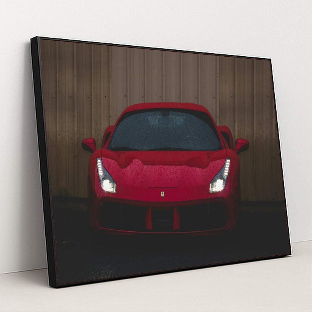 This photo shows the front view of a red Ferrari sports car with headlights on, parked on wet pavement near a metal wall, in a black frame.