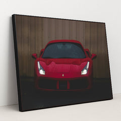 This photo shows the front view of a red Ferrari sports car with headlights on, parked on wet pavement near a metal wall, in a black frame.
