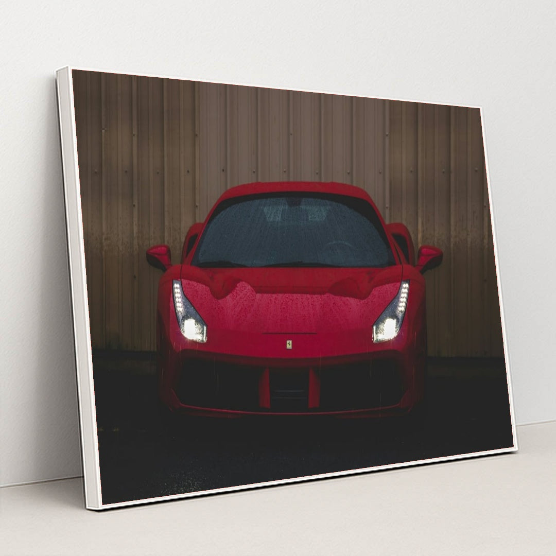 This photo shows the front view of a red Ferrari sports car with headlights on, parked on wet pavement near a metal wall, in a white frame.