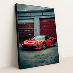 This photo shows a red Ferrari F8 Tributo parked in front of weathered red garage doors on a cloudy day, in a black frame.