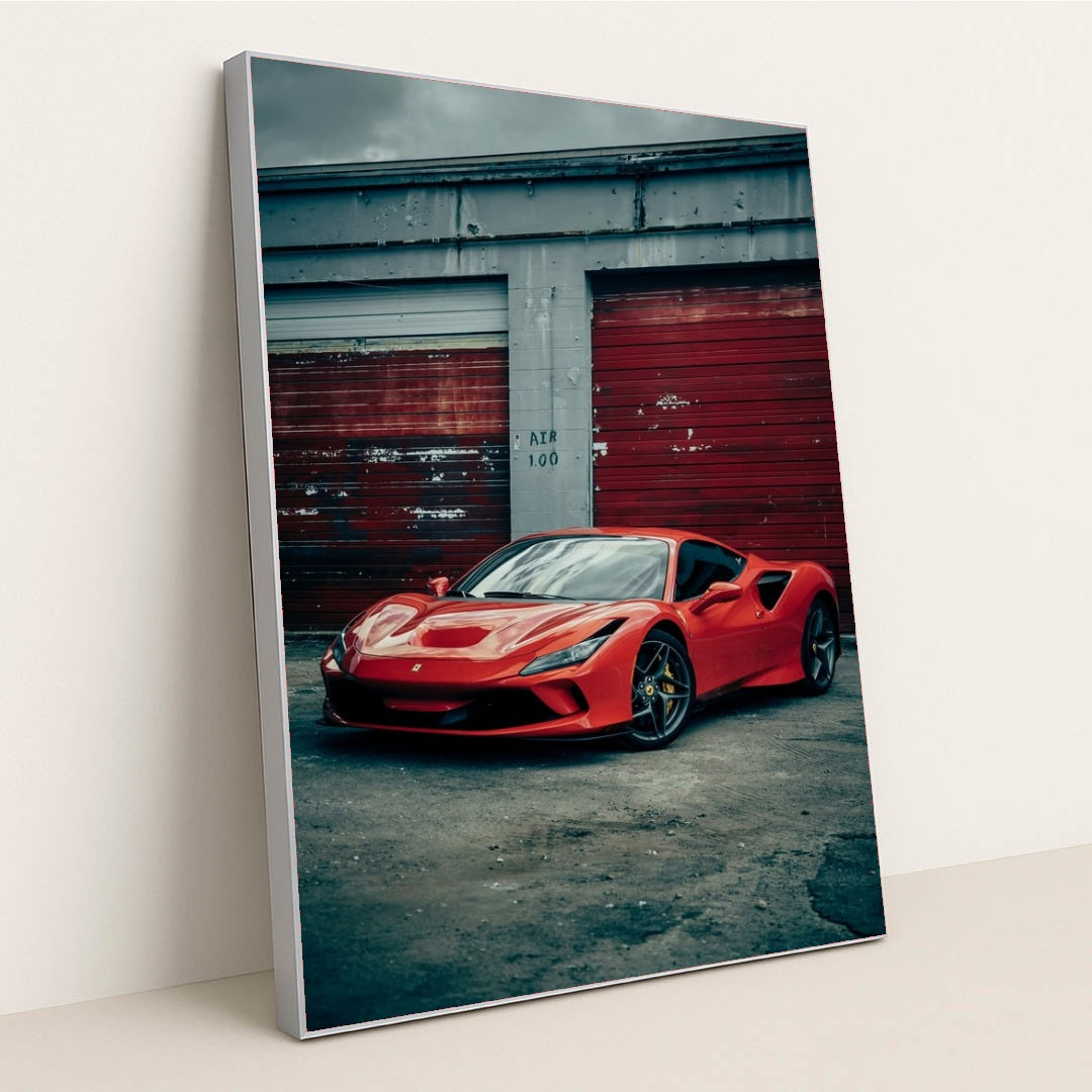 This photo shows a red Ferrari F8 Tributo parked in front of weathered red garage doors on a cloudy day, in a silver frame.