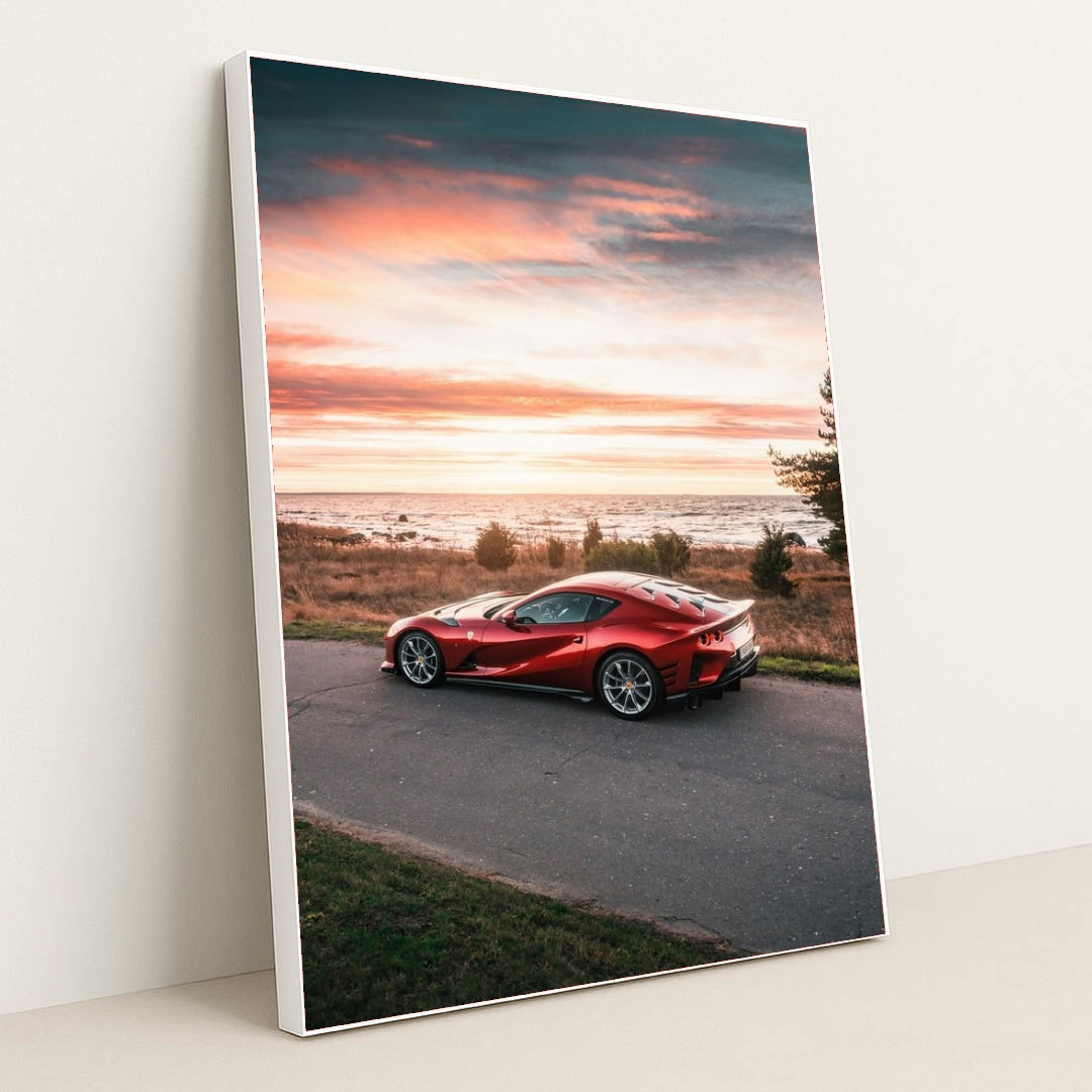 This photo shows a red Ferrari 812 Superfast parked by the seaside at sunset, in a white frame.