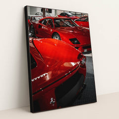 This photo shows a group of classic red Ferrari supercars displayed indoors on a black grid floor, in a black frame.