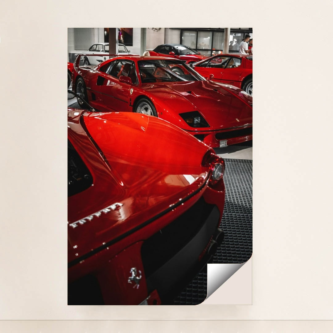 This photo shows a group of classic red Ferrari supercars displayed indoors on a black grid floor, minimalist unframed style.