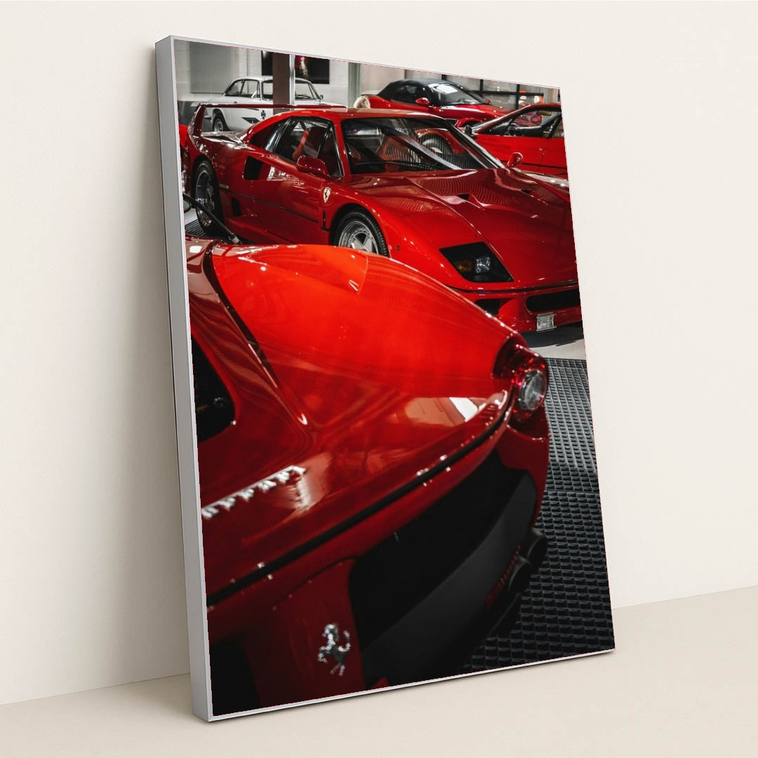 This photo shows a group of classic red Ferrari supercars displayed indoors on a black grid floor, in a silver frame.