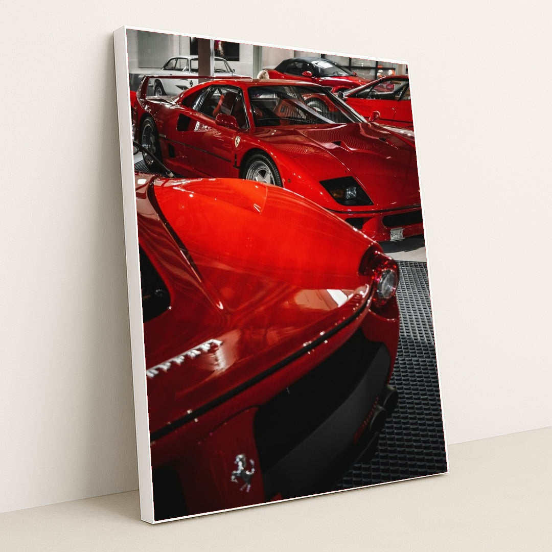 This photo shows a group of classic red Ferrari supercars displayed indoors on a black grid floor, in a white frame.