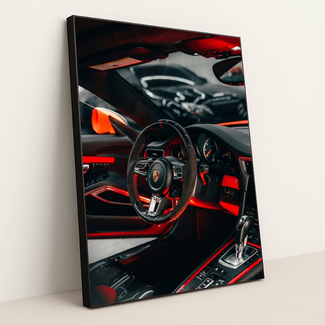 This photo shows the interior of a Porsche with a black and red steering wheel, paddle shifters, and orange accents, in a black frame.