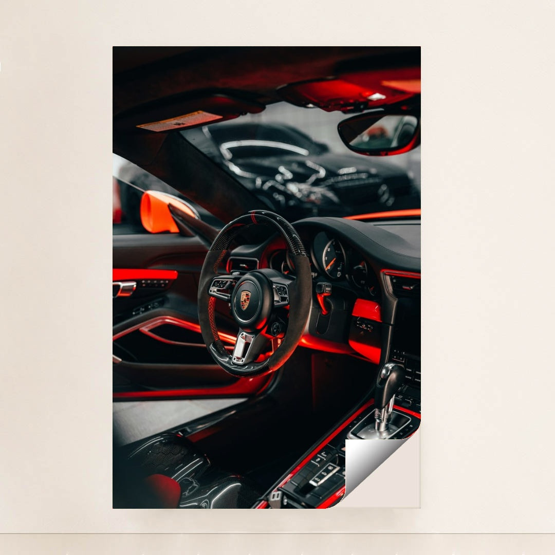This photo shows the interior of a Porsche with a black and red steering wheel, paddle shifters, and orange accents, minimalist unframed style.