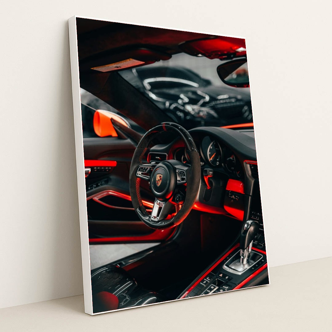 This photo shows the interior of a Porsche with a black and red steering wheel, paddle shifters, and orange accents, in a white frame.