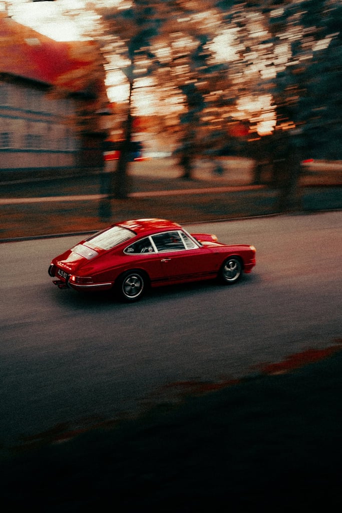 Porsche in Motion Through Autumn Hues, sleek red car moving down a tree-lined street, perfect for car wall art.