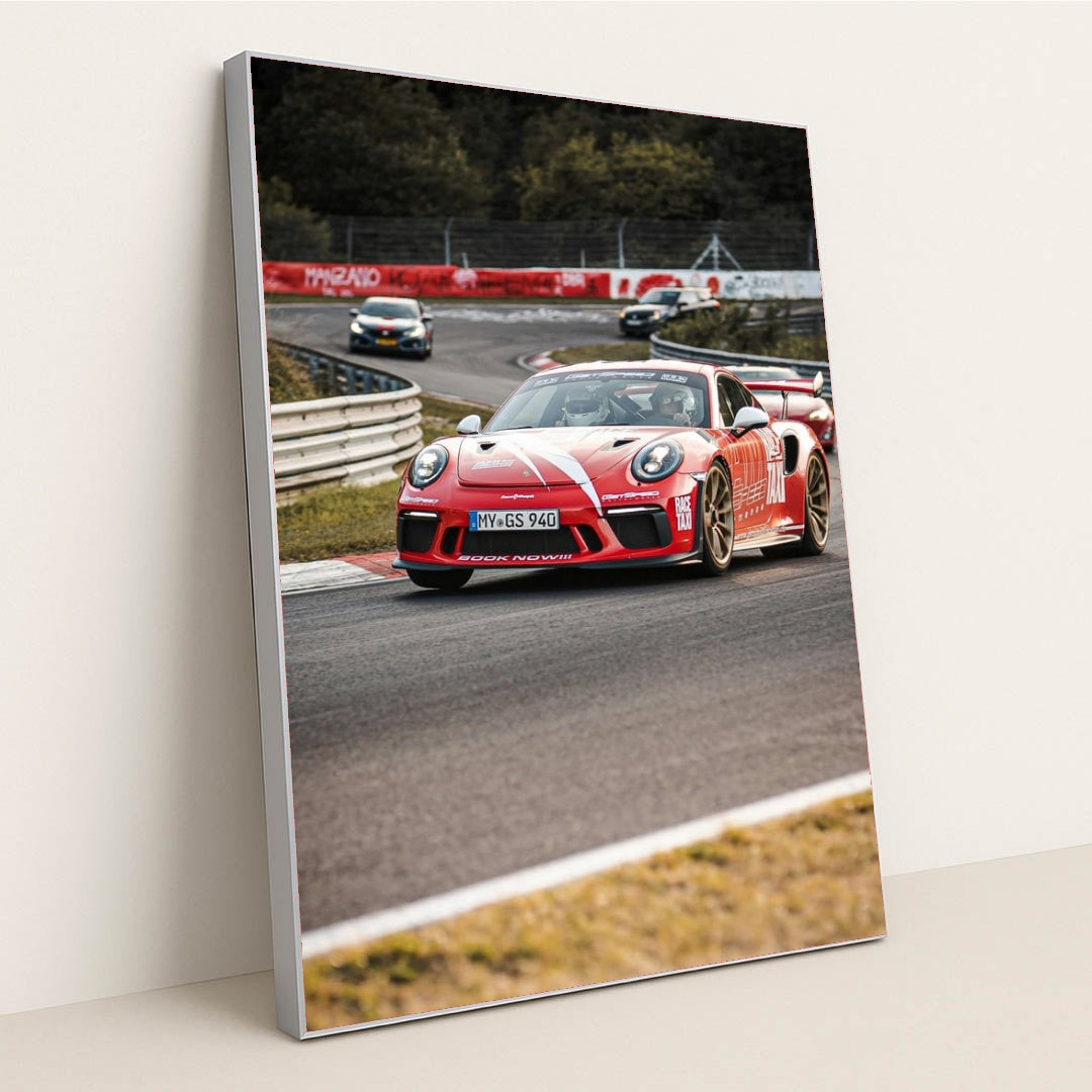 This photo shows a red Porsche GT3 RS race car with white stripes driving on a track during a motorsport event, in a silver frame.