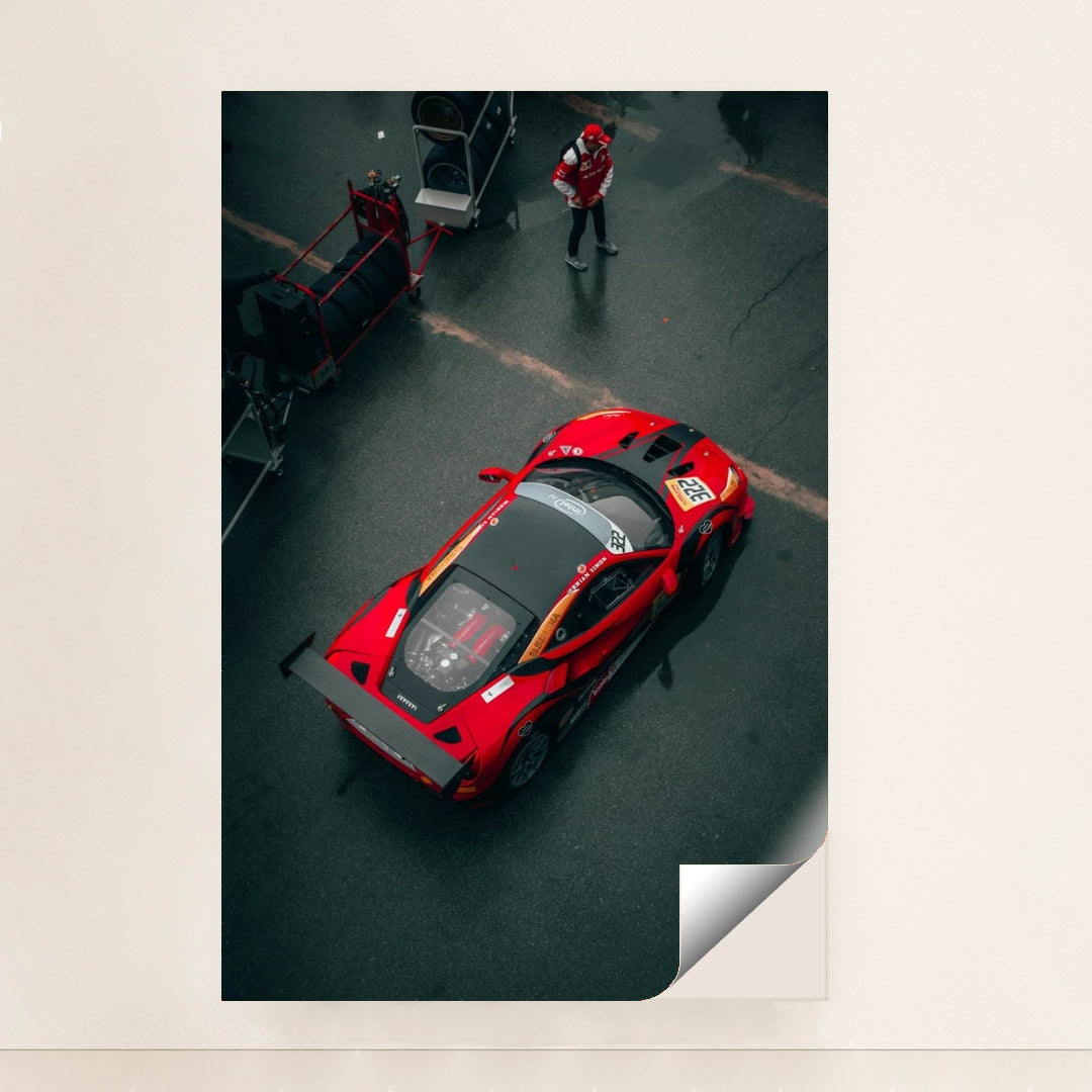 This photo shows an overhead view of a red Ferrari race car with a large rear wing parked in the pit lane, unframed style.