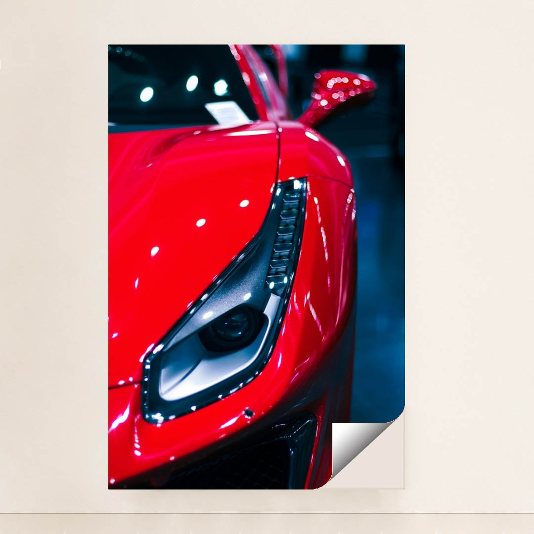 This photo shows a close-up of the left headlight and front fender of a red Ferrari under bright lights, minimalist unframed style.