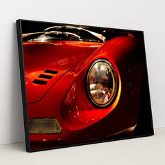 This photo shows a close-up of the front left headlight and fender of a classic red Ferrari Dino, in a black frame.