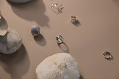 cottonbro studio - Minimalist arrangement of silver rings on a beige background with stones and a feather.