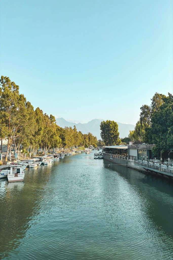 Hasan Hüseyin Korkmaz - Tranquil river scene in Hatay, Türkiye with anchored boats and lush greenery under a clear blue sky.