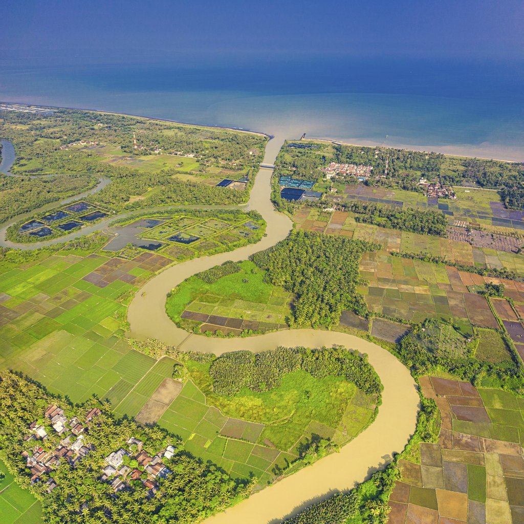 Tom Fisk - A breathtaking aerial view of lush farmland, meandering river, and coastal areas under a clear blue sky.