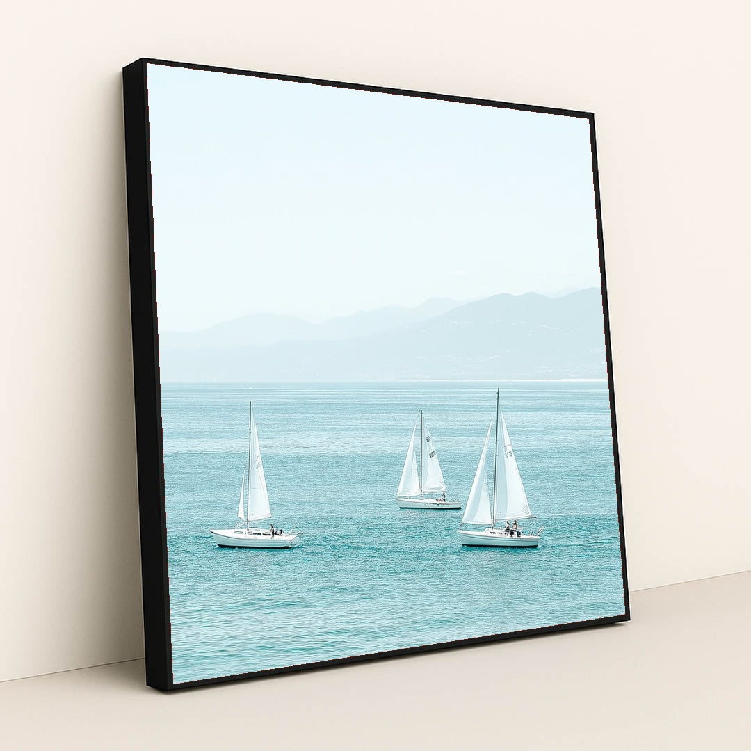This artwork shows three white sailboats on calm turquoise water with mountains in the distance, in a black frame.