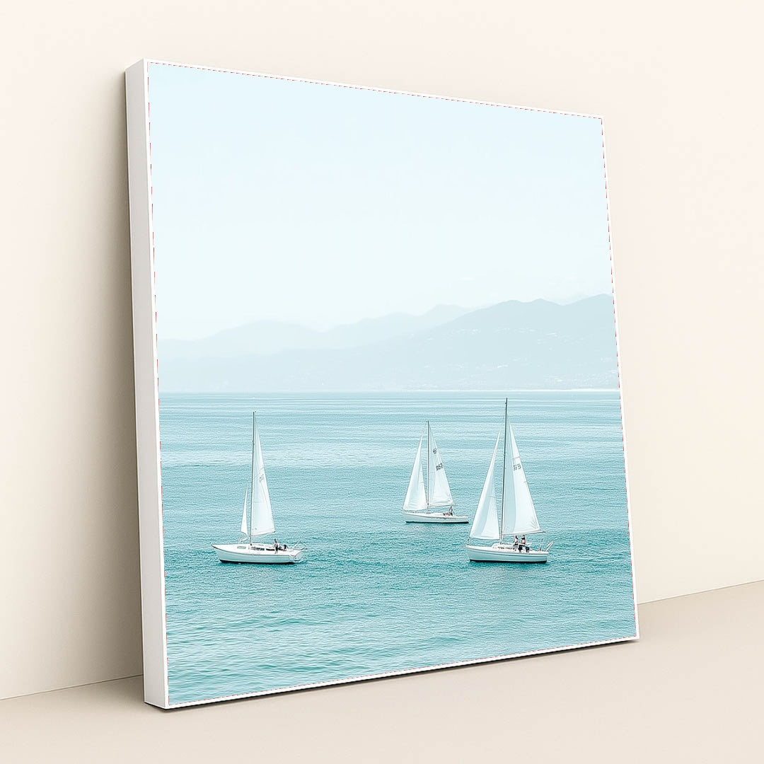 This artwork shows three white sailboats on calm turquoise water with mountains in the distance, in a white frame.