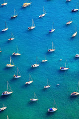 This artwork features an aerial view of moored sailboats on bright blue water.