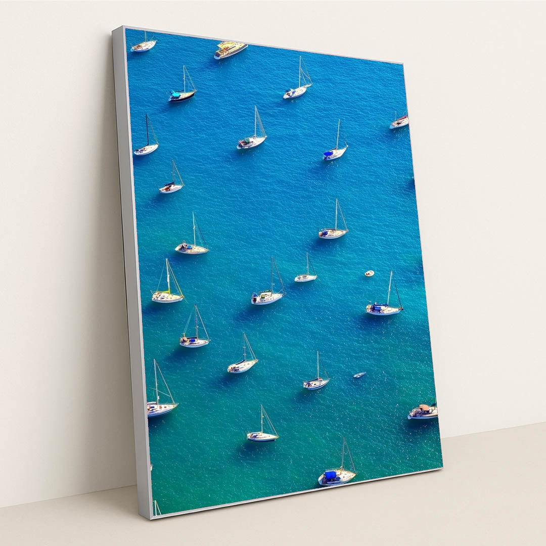 This artwork features an aerial view of moored sailboats on bright blue water, in a silver frame.