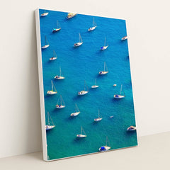 This artwork features an aerial view of moored sailboats on bright blue water, in a white frame.