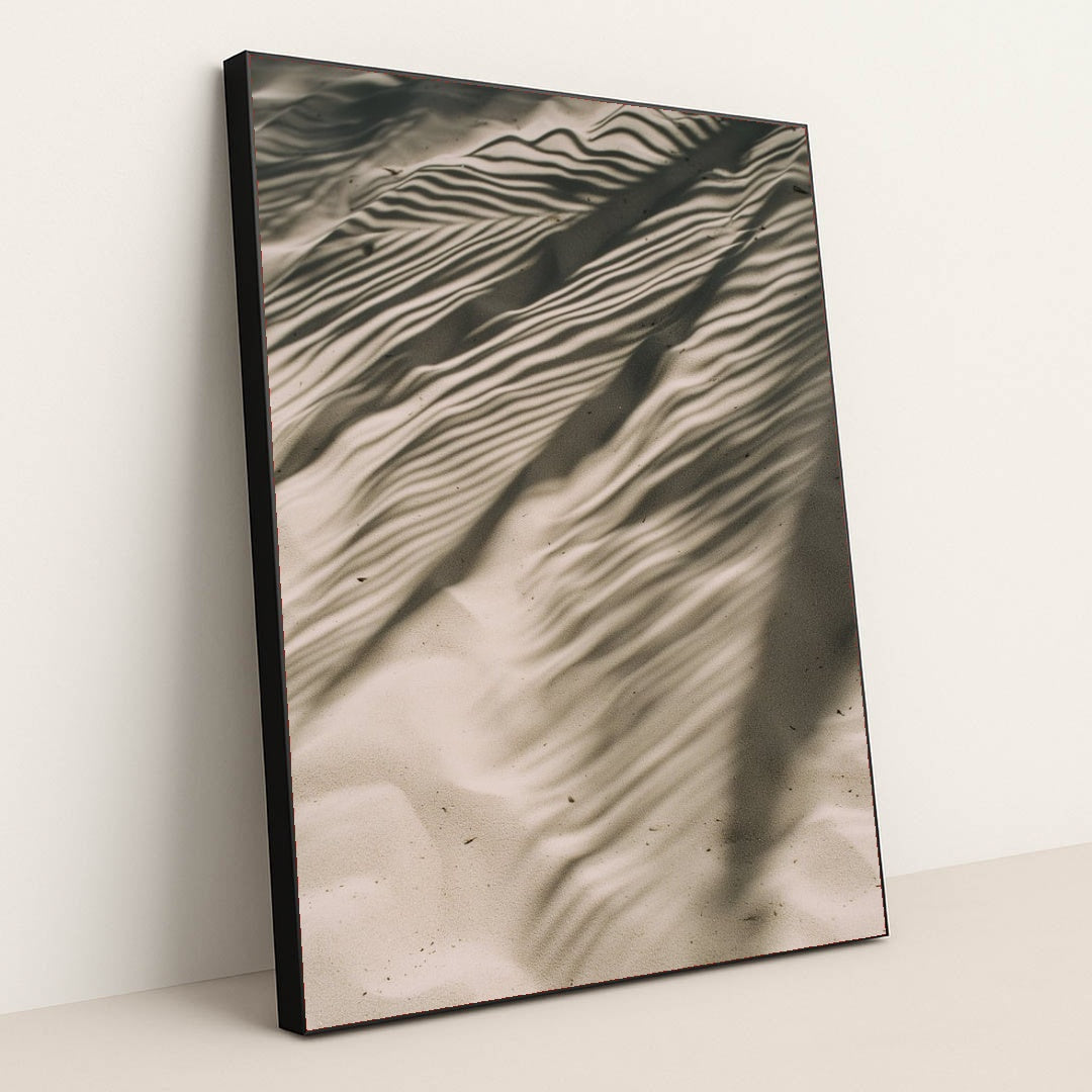 This artwork features rippled sand with striking palm leaf shadows, creating an abstract natural pattern, displayed in a black frame.