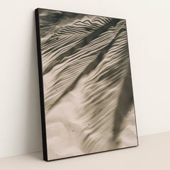 This artwork features rippled sand with striking palm leaf shadows, creating an abstract natural pattern, displayed in a black frame.