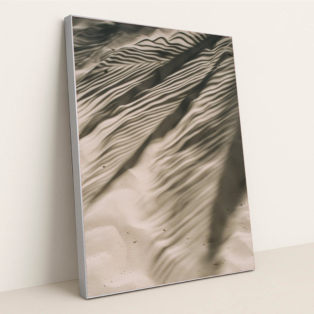 This artwork features rippled sand with striking palm leaf shadows, creating an abstract natural pattern, displayed in a silver frame.