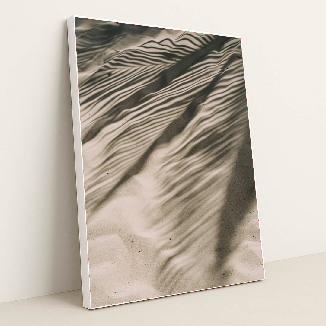 This artwork features rippled sand with striking palm leaf shadows, creating an abstract natural pattern, displayed in a white frame.