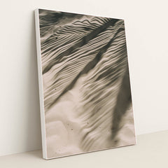 This artwork features rippled sand with striking palm leaf shadows, creating an abstract natural pattern, displayed in a white frame.