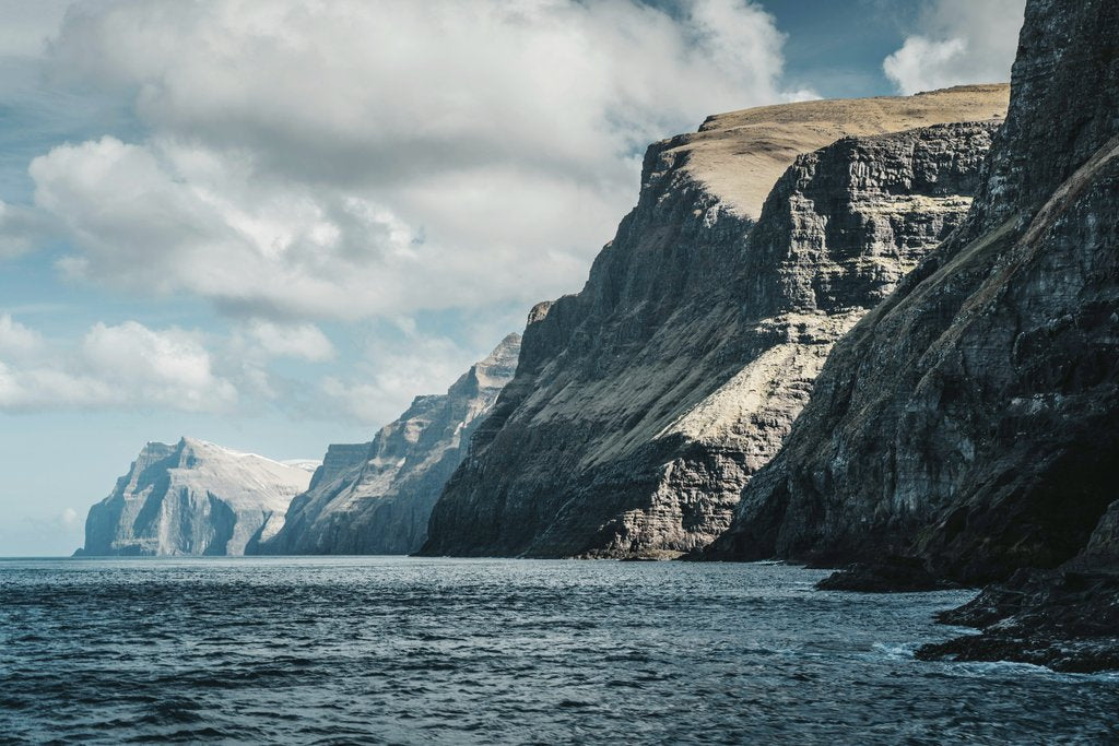 Raul Ling - Majestic cliffs rise from the ocean under a cloudy sky, showcasing nature's grandeur and beauty.
