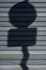 Victor  Moragriega - Abstract shadow of a sign on a metal shutter, creating a dramatic visual contrast.