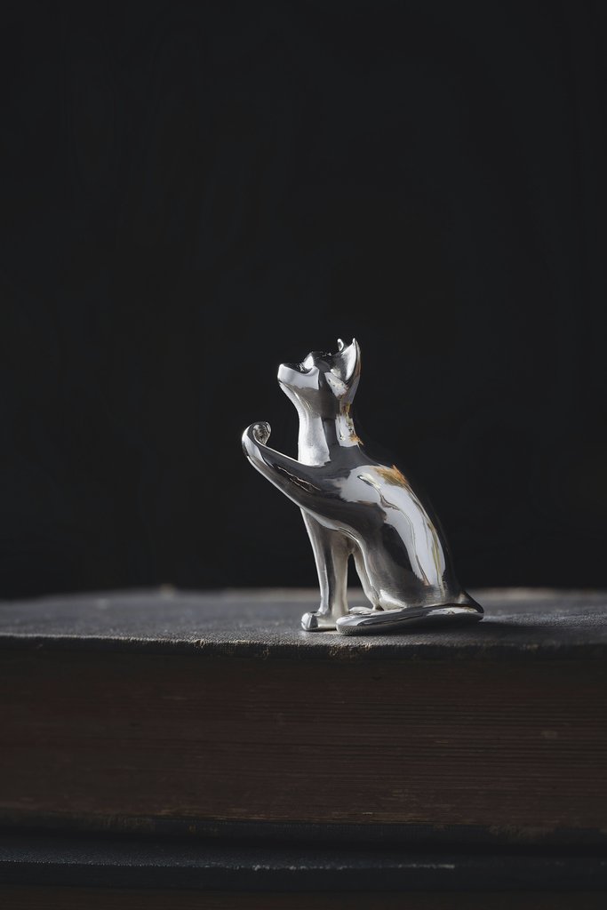 COPPERTIST WU - A minimalist silver cat figurine placed on an old book with a dark background.
